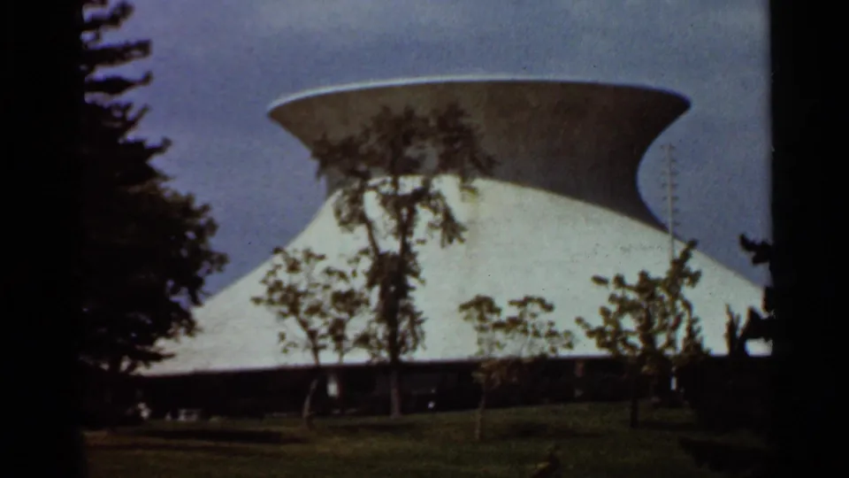 A modernist building with a wide saucer-like roof appears beyond trees in the Saint Louis 1966 home-movie clip.