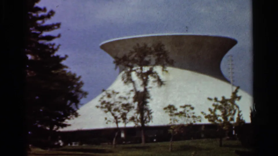 1966 St. Louis home-movie frame showing a white modernist exterior with a saucer-like roof, lawn, and trees.