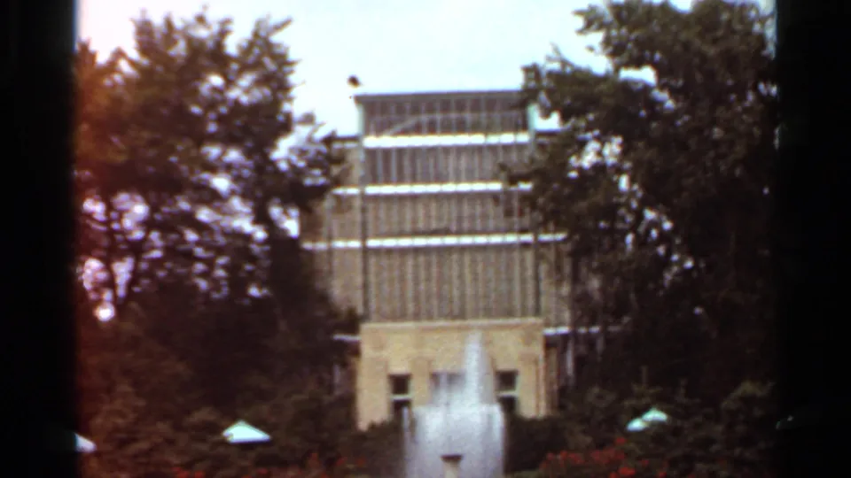 1966 St. Louis home-movie frame showing a more traditional facade behind trees and a foreground fountain.
