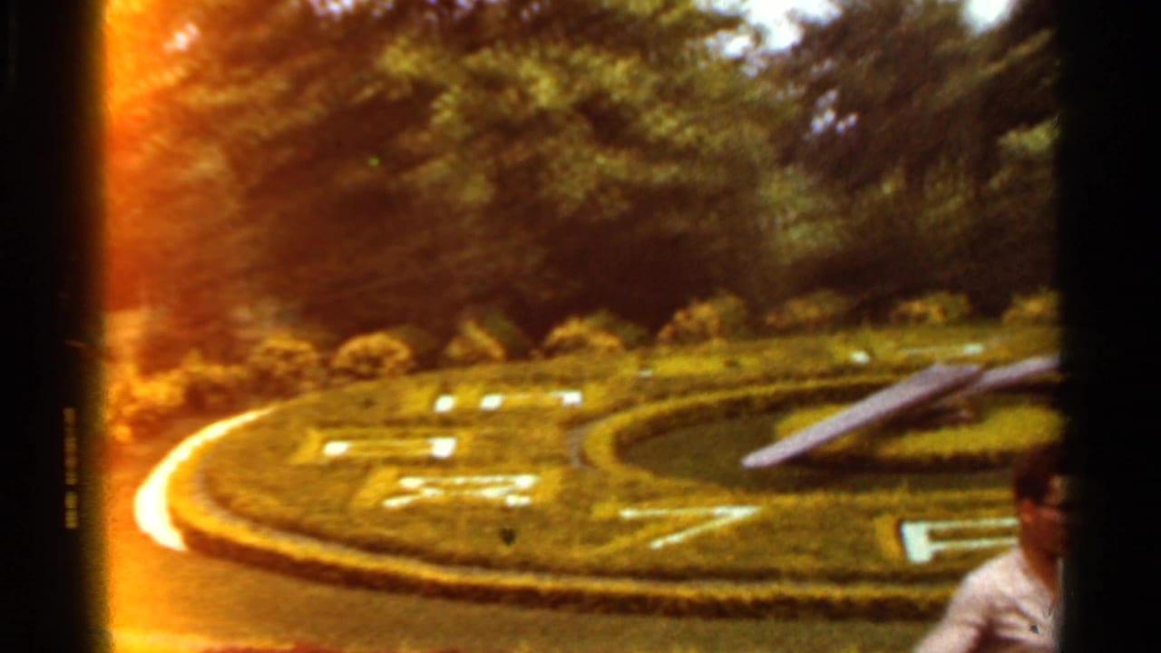 Floral clock in a landscaped park with a partially visible man at the right edge.