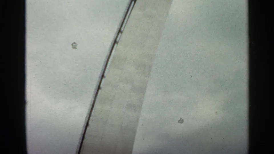 1966 Saint Louis home-movie frame of an unfinished concrete structure with a scaffold line and visible 8mm film specks.