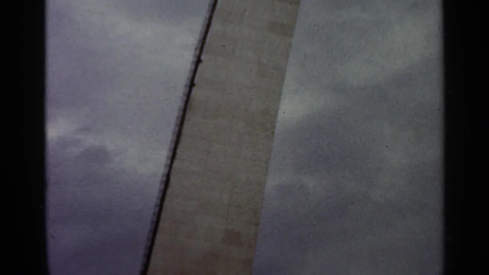 Final 1966 Saint Louis construction frame with the scaffold curving beside a tall unfinished concrete surface under cloudy sky.