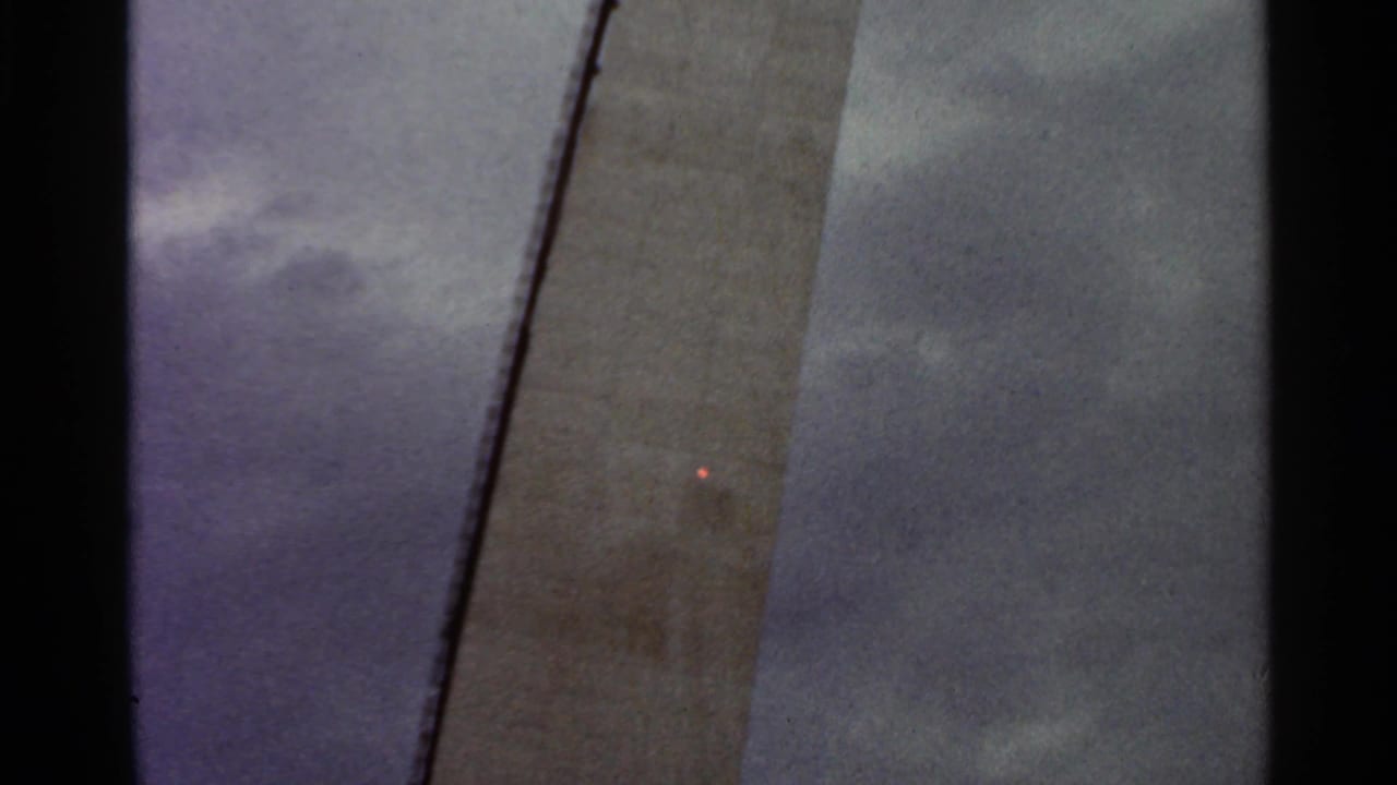 Tall concrete structure seen against a cloudy sky with dark film borders.
