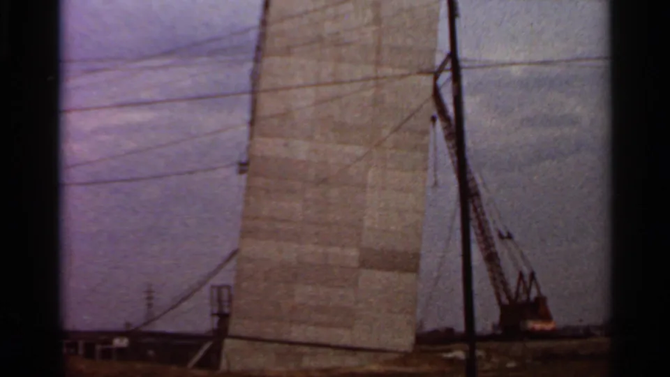 1966 Saint Louis construction view with a tall concrete form, crane silhouettes, overhead wires, and low city buildings.