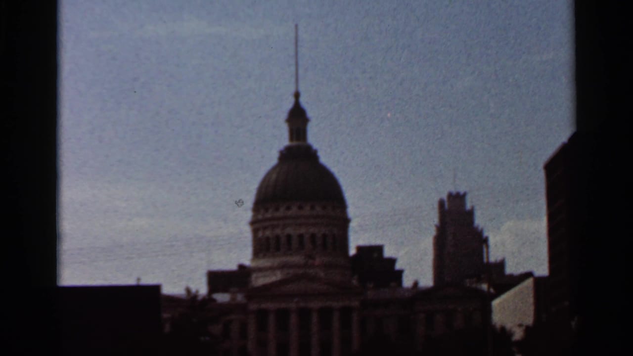 Domed historic building silhouette on a city skyline under pale blue sky.