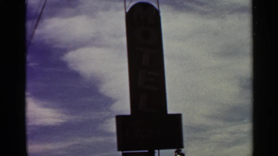 Tall motel sign in 1966 St. Louis footage, filmed from below against streaked clouds with partial lettering visible.
