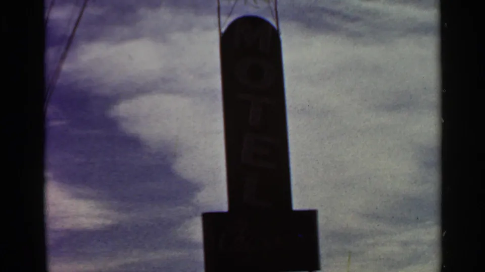 Close view of a roadside motel sign in 1966 St. Louis home-movie footage, with dark silhouette and visible but indistinct business lettering.