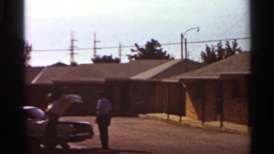 A man in a light shirt stands by an open hood on a classic sedan in a Saint Louis residential parking area, circa 1966 per metadata.