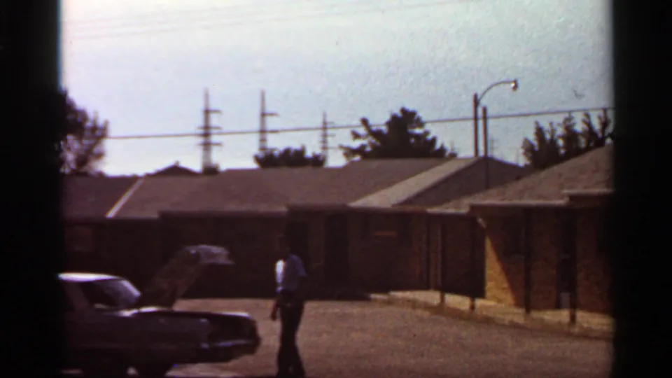 Saint Louis residential-lot view from 1966 metadata, with a man near an open car hood and single-story brick buildings behind him.