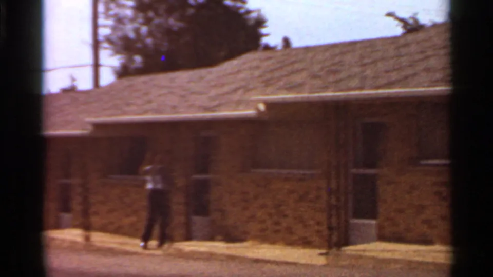 A softer frame shows the adult farther along the brick motel exterior, with the low roof and roadside setting still visible.