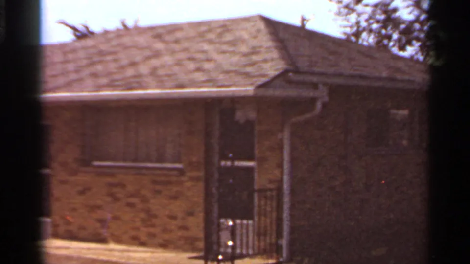 1966 Saint Louis 8mm frame showing a brick apartment exterior with an entry door, small windows, roofline, and tree shadows.