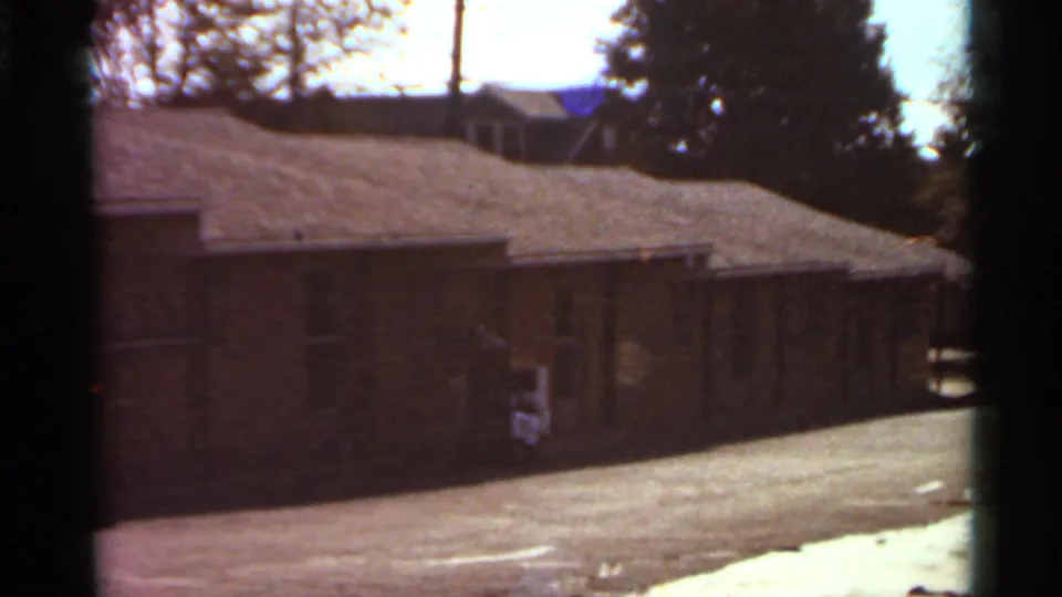 1966 Saint Louis 8mm frame showing the apartment row from a slightly shifted angle, with shaded brick walls and a sunlit drive.