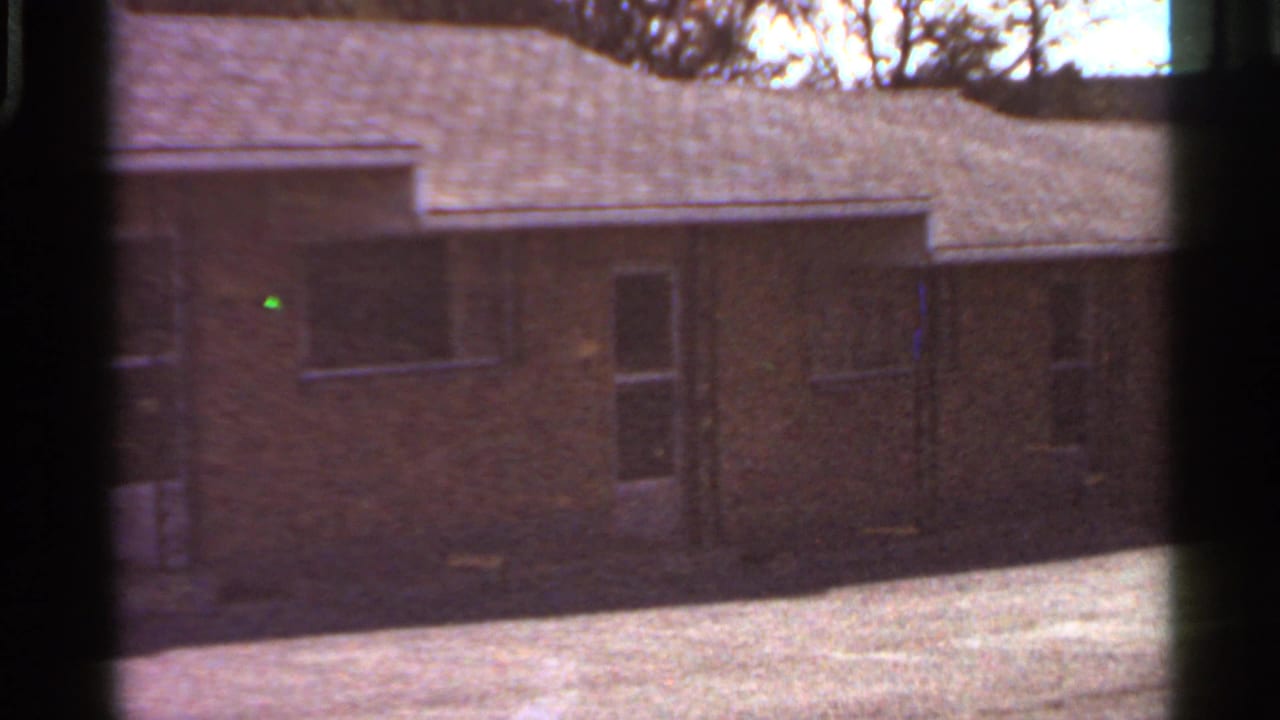 Small brick house seen through dark film-frame edges in bright daylight.