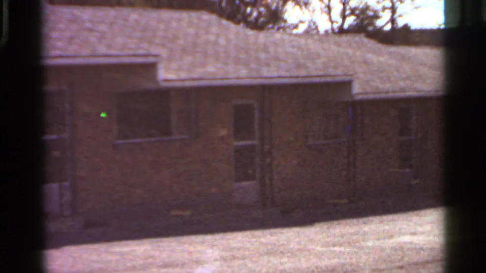 1966 Saint Louis home-movie frame showing a modest brick house with shingled roof and dark 8mm gate edges.