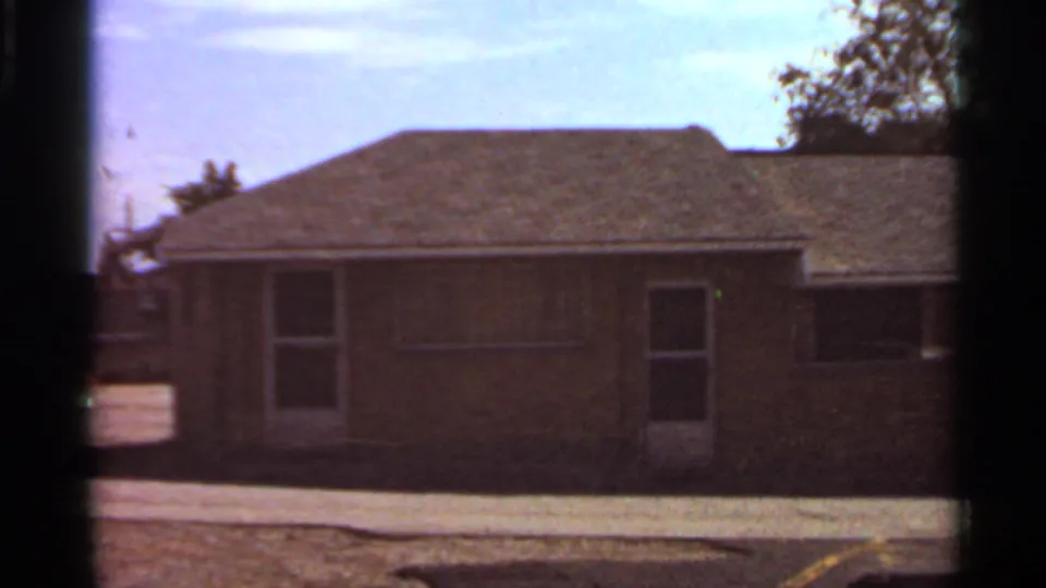 Home-movie frame of a 1966 Saint Louis brick residence, with a door, windows, roofline, and visible 8mm frame edge.