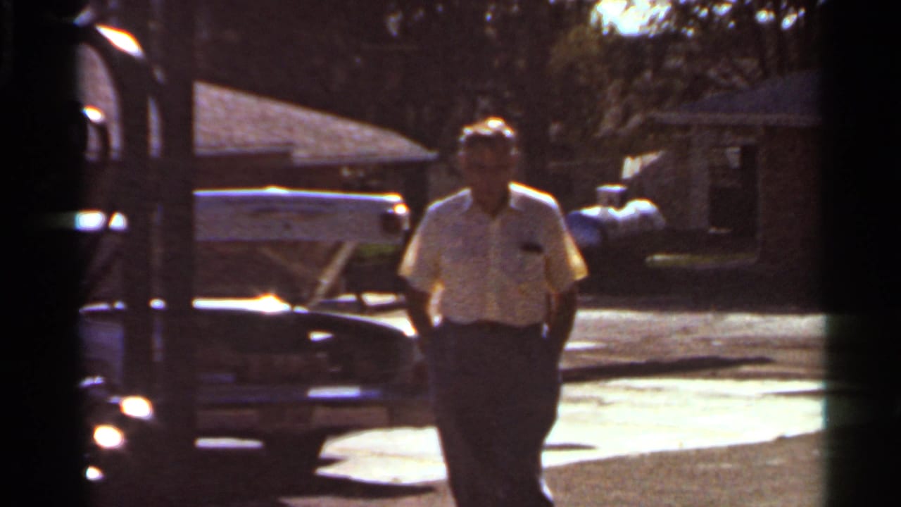 Man walking beside a parked car on a sunlit residential street.