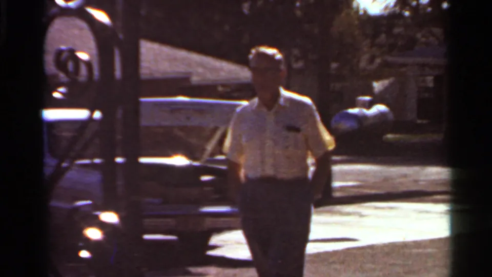 Adult man walks toward the camera on a Saint Louis street, with a parked car and residential buildings behind him.
