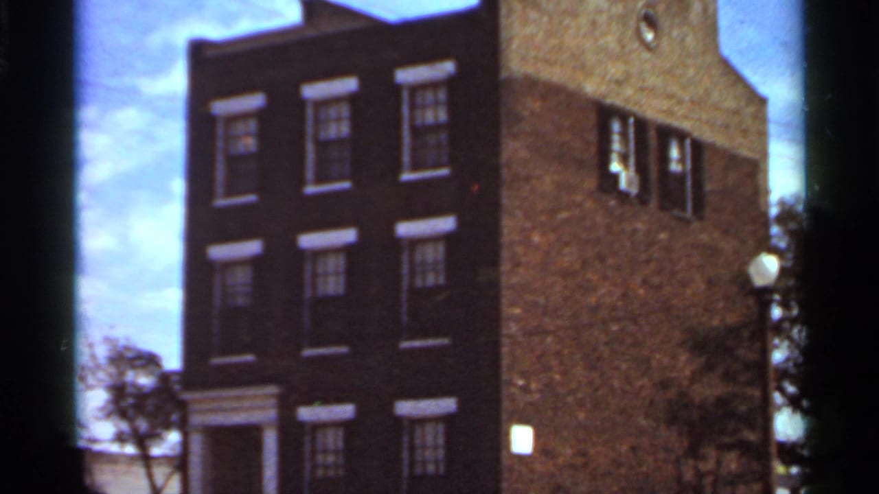 1966 Saint Louis 8mm frame showing a tall brick building with multiple windows, a side wall, sky, and partial tree edge.
