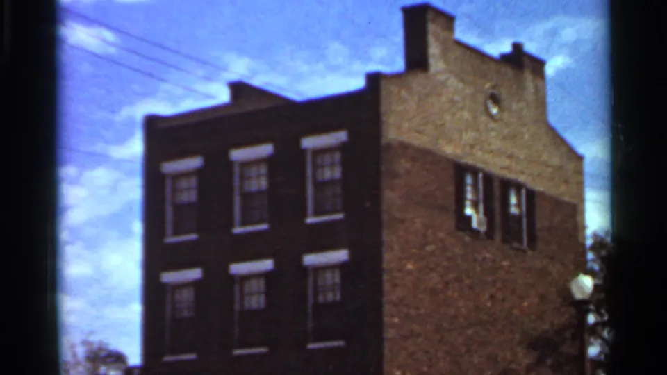 1966 Saint Louis frame of the brick building from a slightly shifted angle, showing windows, side wall, overhead wires, and sky.