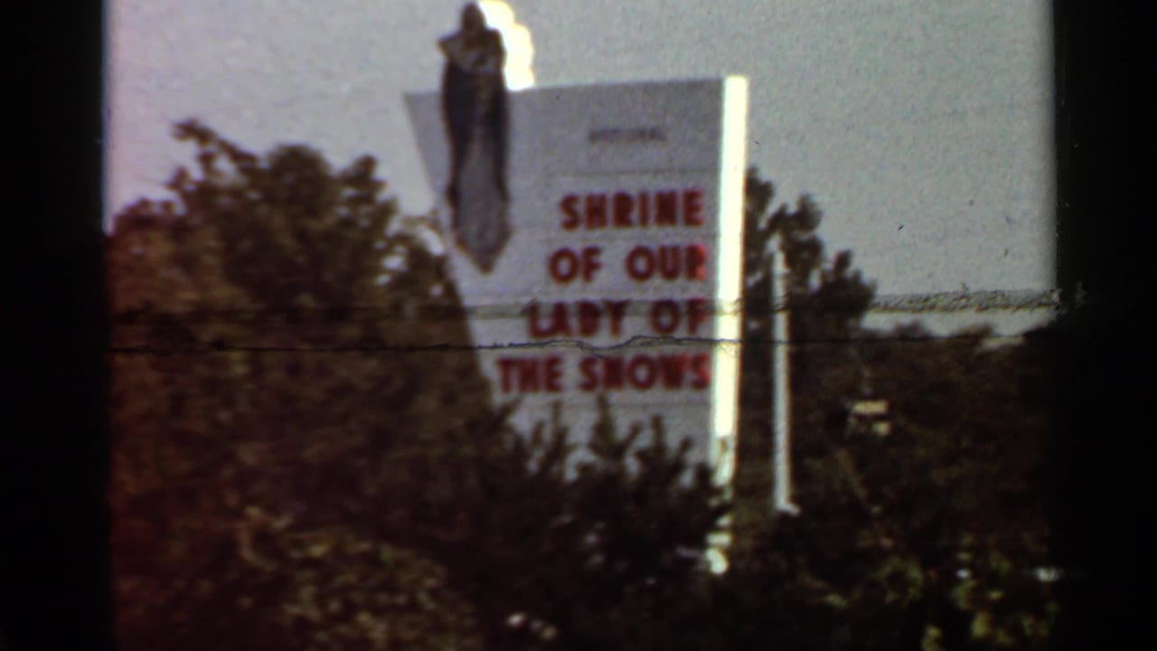 Roadside sign for the Shrine of Our Lady of the Snows with a statue above it.