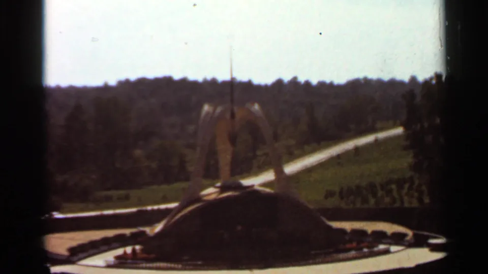 1966 8mm view of a modernist shrine structure at the Shrine of Our Lady of the Snows, seen across lawns, paths, and wooded hills.