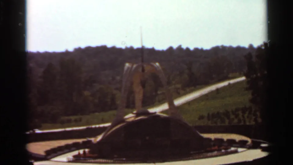 1966 8mm frame of the Shrine of Our Lady of the Snows grounds, with the outdoor shrine centered against lawns, trees, and rolling hills.