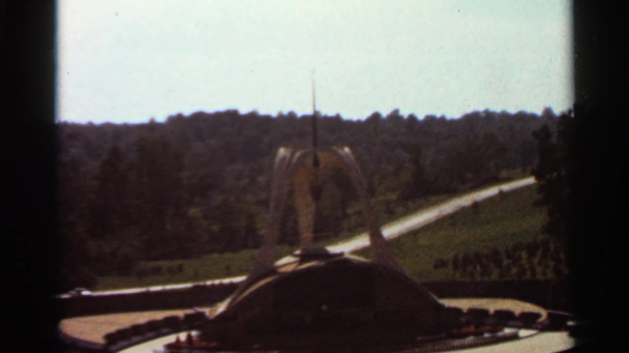Sculptural fountain with a central spire seen across landscaped grounds and dark 8mm frame borders.