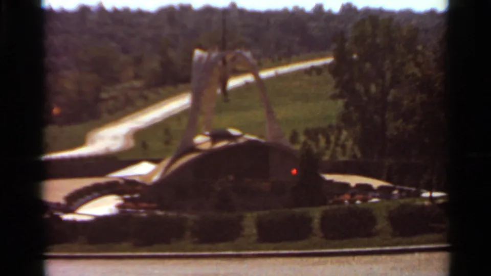 1966 Saint Louis 8mm frame of the curved decorative fountain and central spire against rolling green grounds and trees.