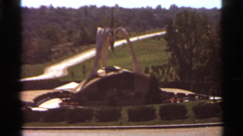 Saint Louis 1966 home-movie still showing the futuristic fountain from a slightly shifted angle within landscaped grounds.
