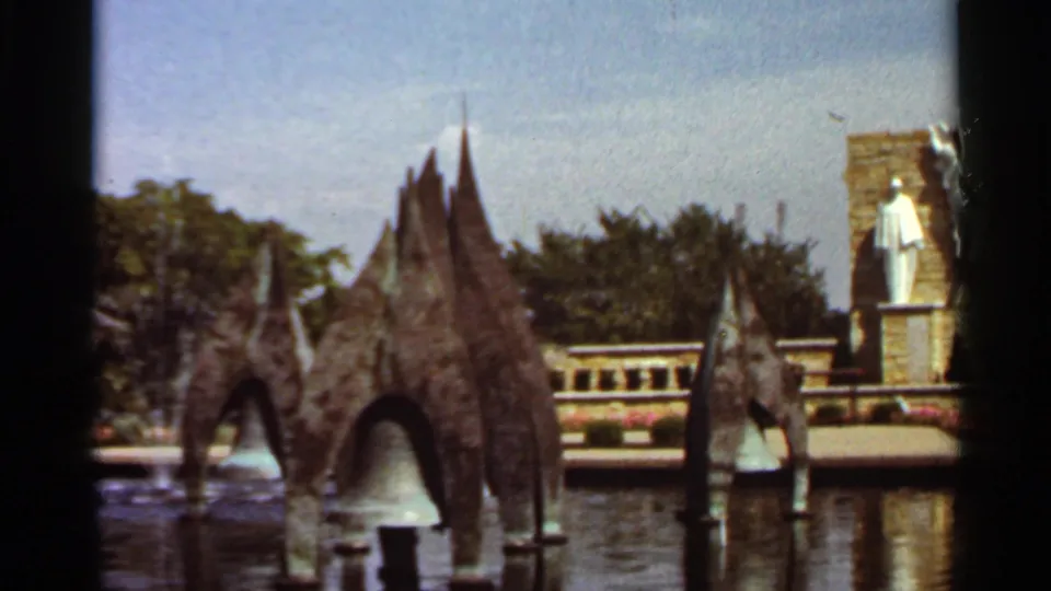 1966 Saint Louis home-movie still centered on a large sculptural fountain element, with reflective water, railings, trees, and a white statue in the background.