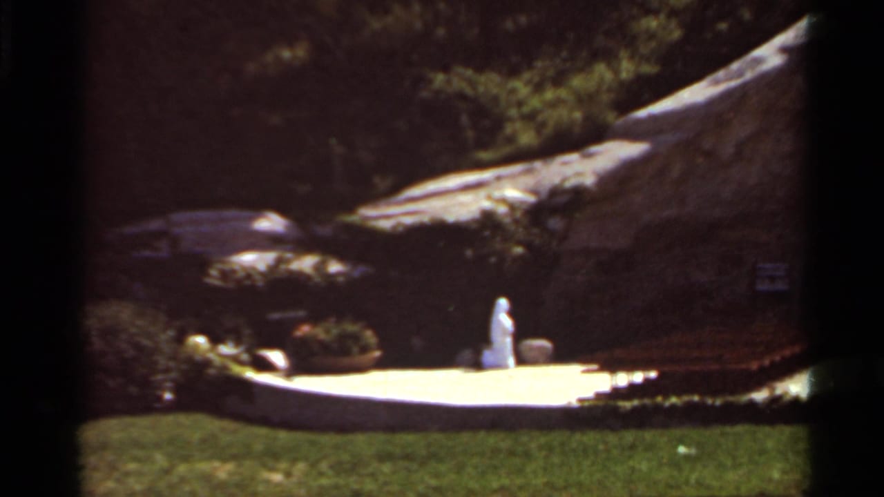 White statue on a sunlit platform before a large rock formation and trees.