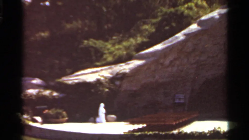 The camera view shifts right across the Saint Louis garden, with a white figure, benches, and a dark cave-like opening in the rock.