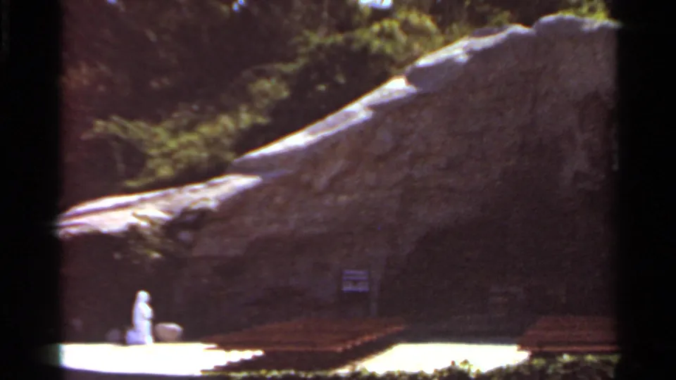 A closer 8mm view of the landscaped rock structure shows benches at its base and the white figure partly visible at frame left.