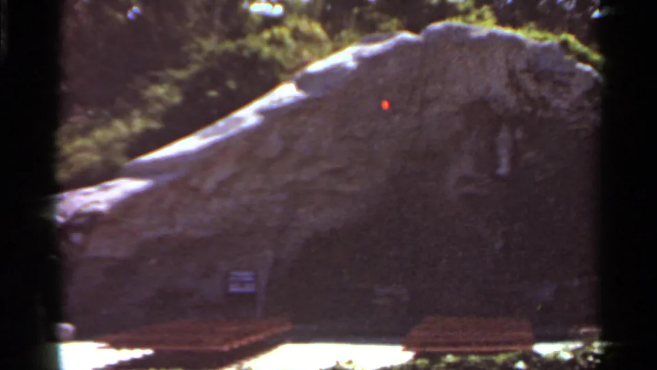 The final frame centers the large rock formation, bench seating, foliage, and a shadowed entrance in the Saint Louis garden scene.
