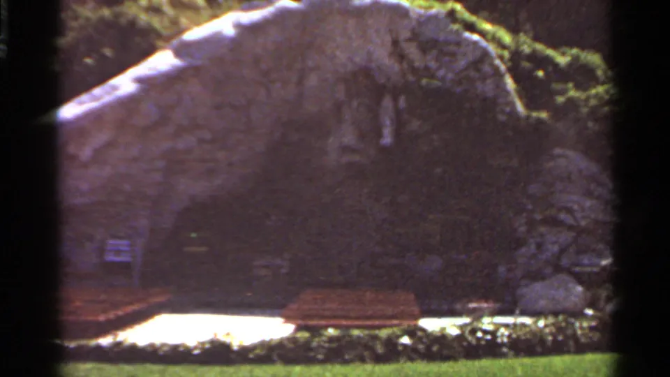 1966 Saint Louis outdoor frame with a brown bench below a weathered rock feature and patches of strong sunlight.
