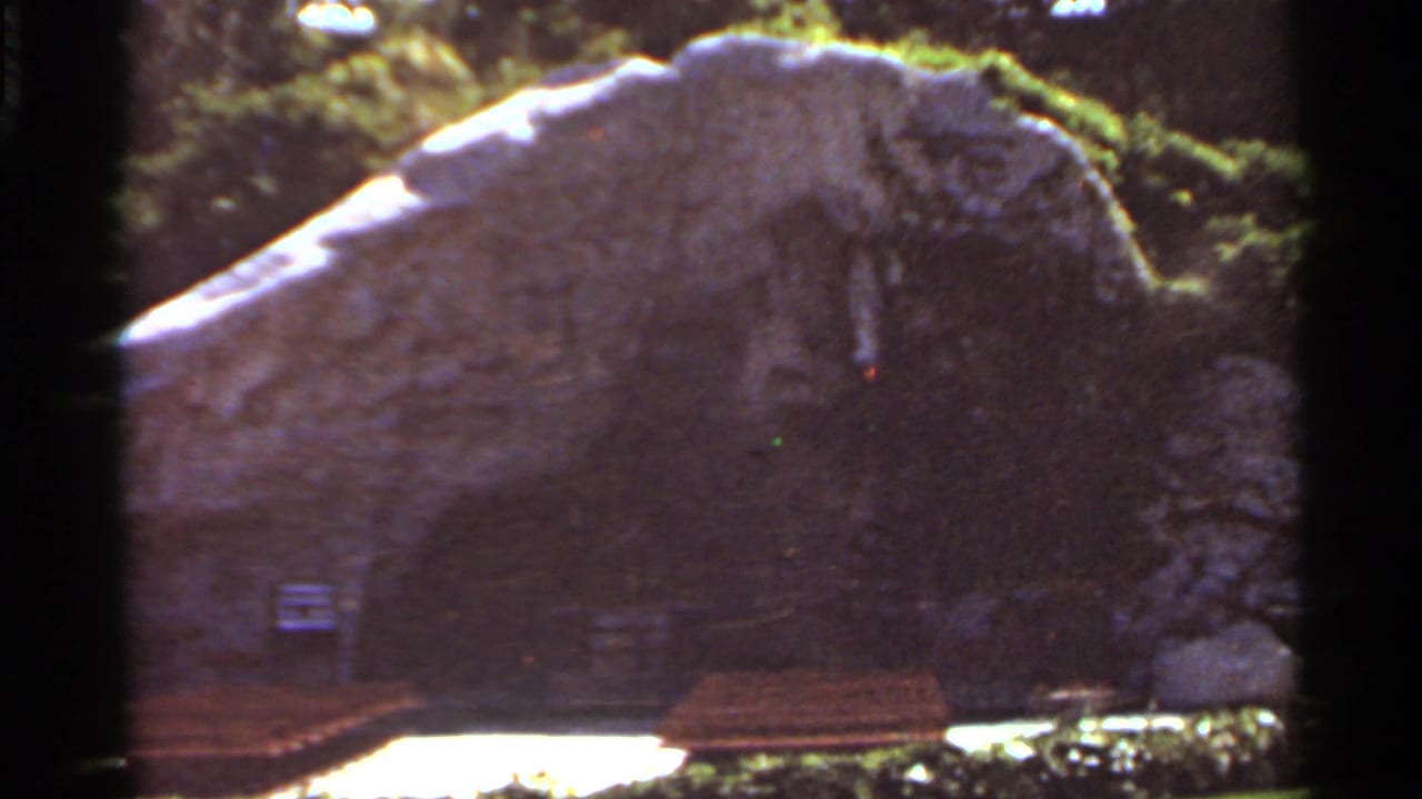 Stone grotto with benches and garden greenery, seen through dark 8mm frame borders.