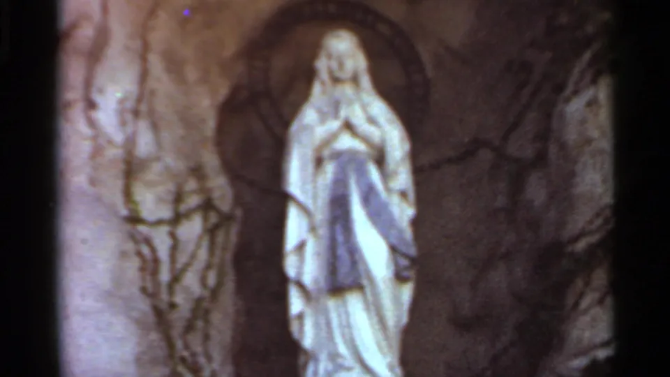 Close 1966 Saint Louis home-movie view of the Marian statue in the grotto, with vines, stone texture, and dark film borders visible.