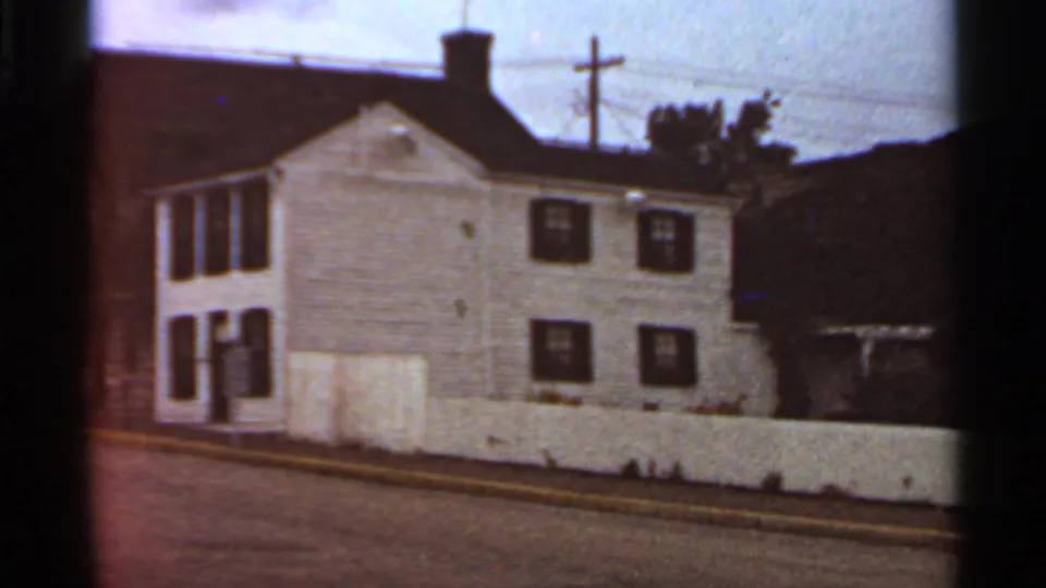 1966 8mm view in Missouri of the Mark Twain Home and Museum exterior, a white clapboard house with dark shutters and low fence.