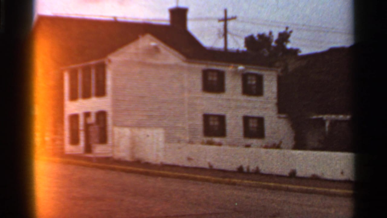 1966 St. Louis home-movie frame showing a white clapboard house, dark shutters, chimney, street edge, and white fence.