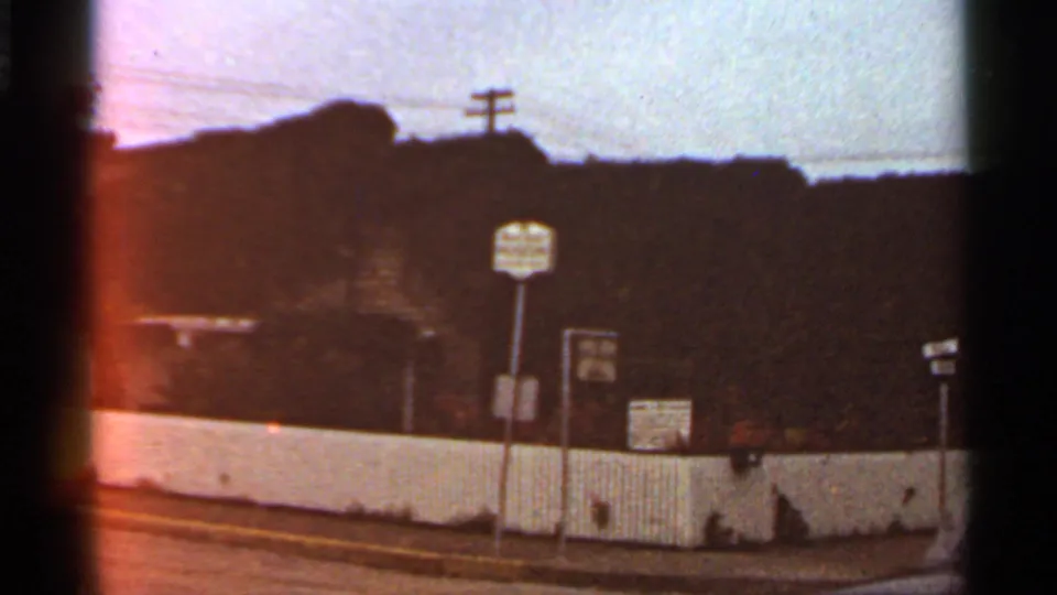 1966 St. Louis frame with a white roadside fence, utility poles, several signs, and a dark background beyond the street.