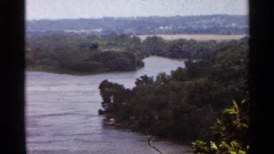 Elevated 1966 Saint Louis-area home-movie view of a curving river channel, dense trees, and distant open land.