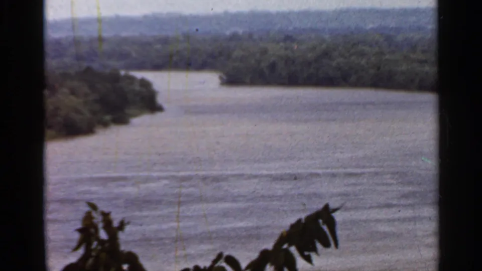 1966 Saint Louis-area 8mm river landscape with open water, tree-lined banks, distant hills, and foreground leaves.