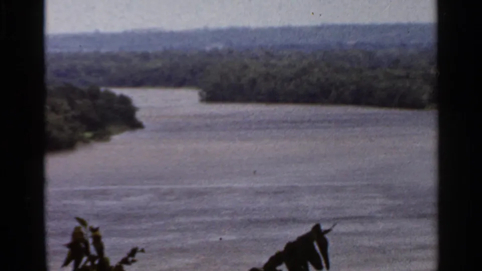 1966 8mm frame showing a calm river and forested shoreline near Saint Louis, Missouri, with soft color and home-movie grain.