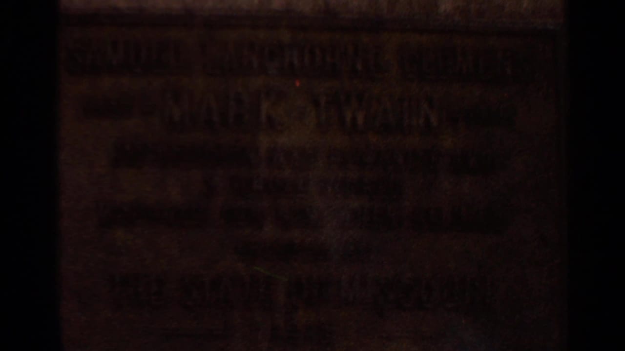 Close home-movie view of a weathered bronze plaque in Saint Louis, with Mark Twain lettering visible through low exposure.