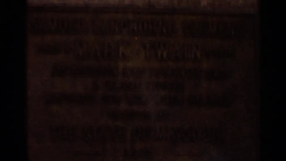 Close home-movie view of a weathered bronze plaque in Saint Louis, with Mark Twain lettering visible through low exposure.
