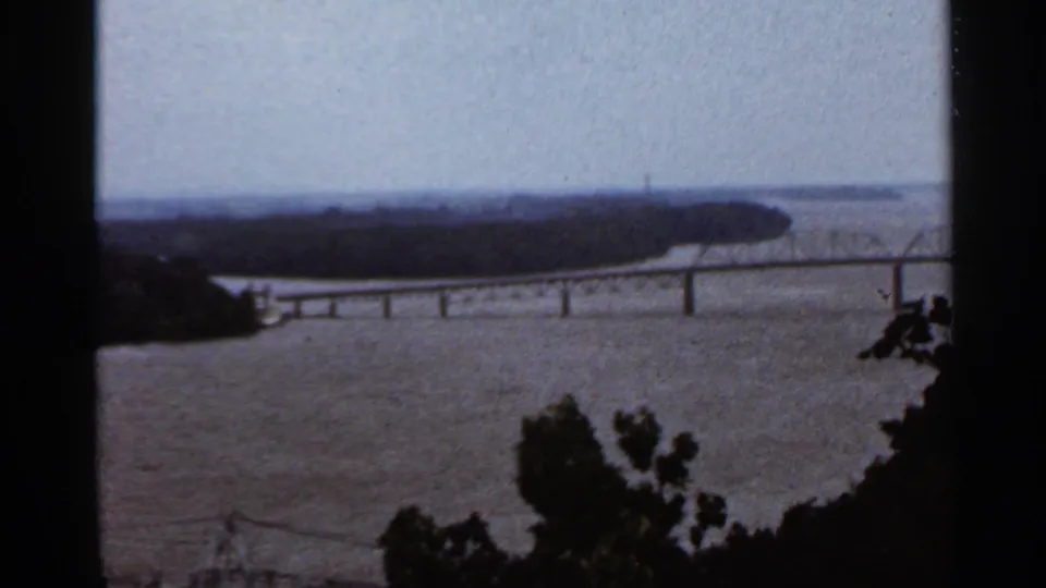 1966 Saint Louis home-movie frame showing a river panorama with overlook railing and distant bridge-like structures.