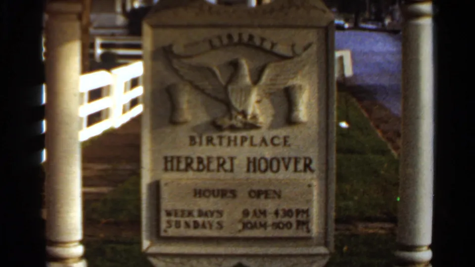 Close 8mm frame of the Herbert Hoover birthplace marker showing carved lettering, eagle emblem, and visiting hours.