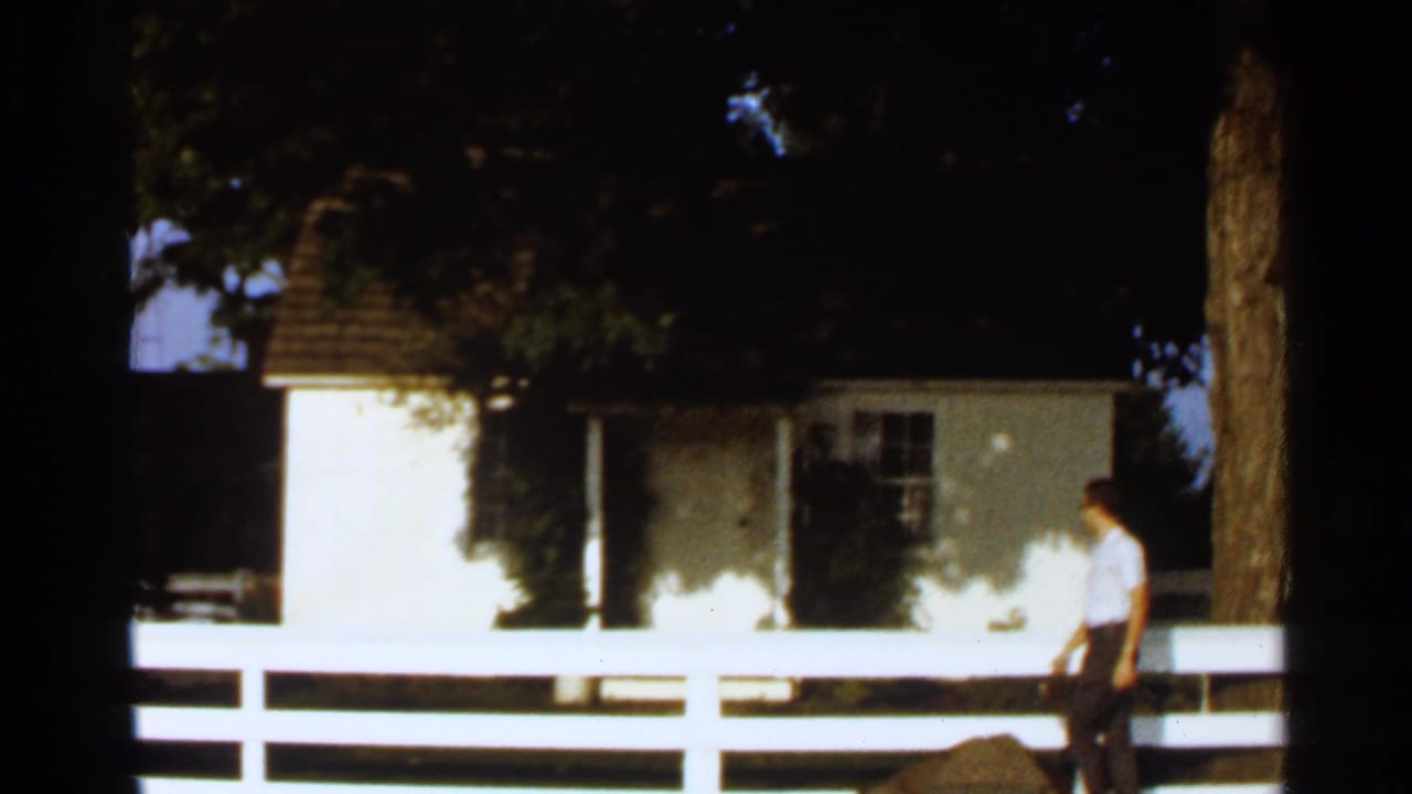Man walking near a small white house behind a white picket fence.