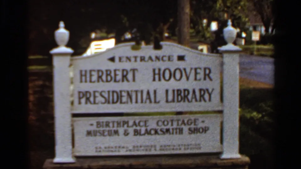 1966 8mm frame with the Herbert Hoover Presidential Library entrance sign centered, surrounded by trees, a driveway, and heritage-site landscaping.