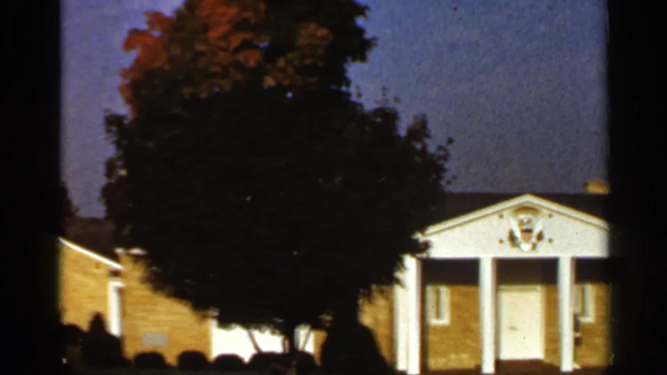 1966 St. Louis home-movie view of a tree with autumn color in front of a brick building and white columned entrance.